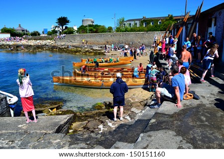 DUBLIN, IRELAND – JUNE 9: Unidentified competitors and onlookers at The East Coast Rowing Council Races on June 9, 2013 in Sandycove, Ireland. Wooden racing skiffs lie along the shoreline.
