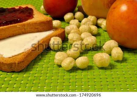 a full breakfast served on a green tablecloth with toast, jam, butter, cheese, peaches, plums, cereals, corn flakes