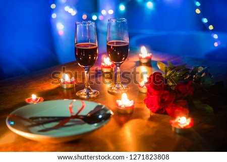 Valentines dinner romantic love concept / Romantic table setting decorated with fork spoon on plate and couple champagne glass roses with candlelight on wooden table dinner night light background