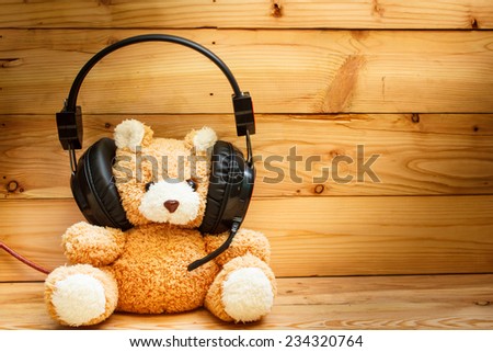 teddy bear with headphones on wood background.