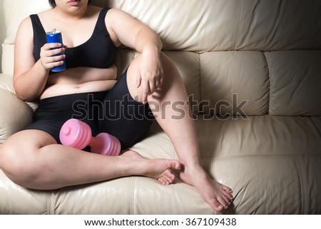fat woman tired give up exercise concept and soft drink in hand drop dumbbell sitting on sofa