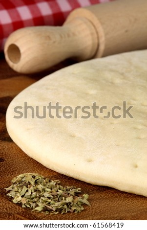 pizza  dough sheeet and fresh oregano  on  wood cutting board with rolling pin