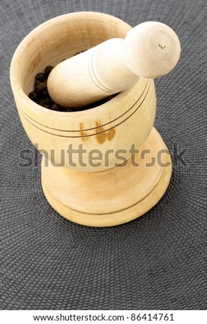 wood mortar and pestle full with aromatic black peppercorns
