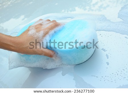 female hand is cleaning  car bonnet with blue sponge; selective focus at hand