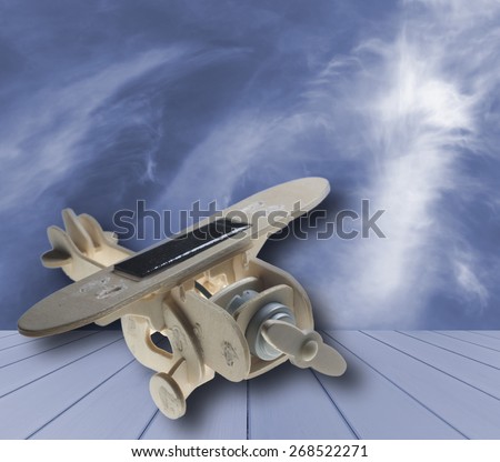 wooden toy airplane with solar panel on blue wood, on  blue sky and cloud background