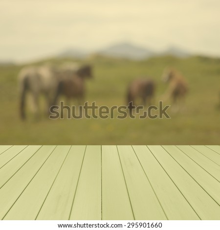 Empty wooden,green deck table with horses in the meadows and mountains in blurred background. UK. Ready for product display montage.