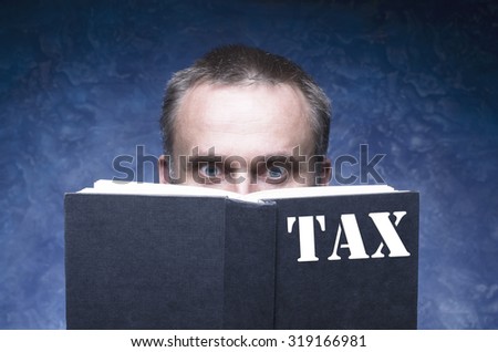 TAX written on the cover of the book, mature man being focused and hooked by book, reading open book