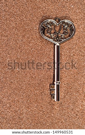 Silver key on sand Silver heart-shaped key on brown sand