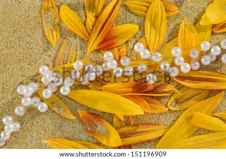 Autumnal feast or wedding decoration background Pearls and colored sunflower leaves on sand background