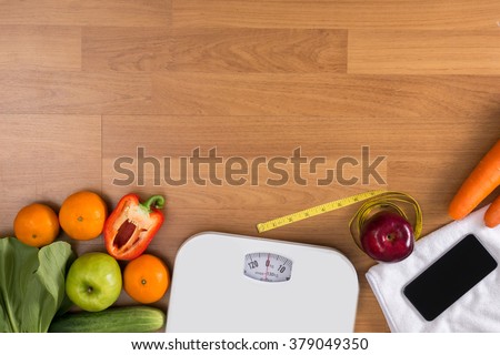 Fitness and weight loss concept, dumbbells, white scale, fruit and tape measure on a wooden table, top view, free copy space