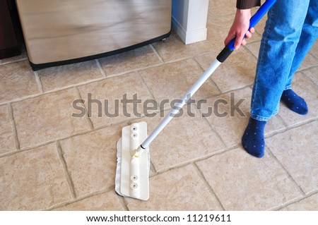 Close-up picture of woman\'s hand holding a mop cleaning kitchen floor