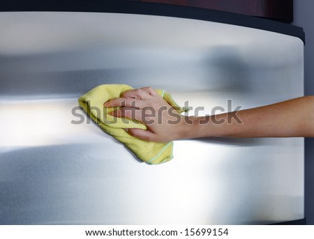 Woman\'s hand with microfiber cloth polishing a stainless steel fridge door