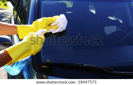 Woman\'s hand with a rag and glass cleaner washing windshield glass of an SUV car