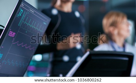 Monitor Showing EKG Reading of a Woman Athlete Running on a Treadmill in the Background, Two Specialists Supervise Exercise, Controlling Physical Activity. Sport Science Theme.