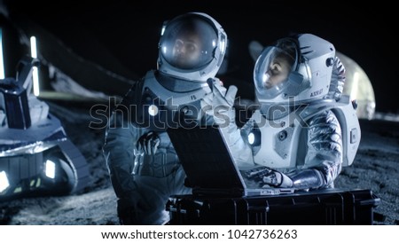 Two Astronauts Wearing Space Suits Work on a Laptop, Exploring Newly Discovered Planet, Send Communicating Signal to Earth. Space Travel, Interstellar Exploration and Colonization Concept.