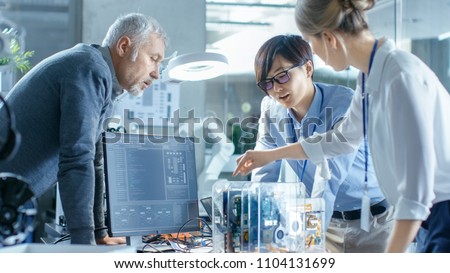 Team of Computer Engineers Choose Printed Circuit Boards to Work with, Computer Shows Programming in Progress. In The Background Technologically Advanced Scientific Research Center.