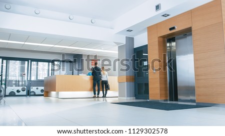 In the Hospital Lobby Young Couple Patients Talks to Receptionist. New, Modern Medical Facility.