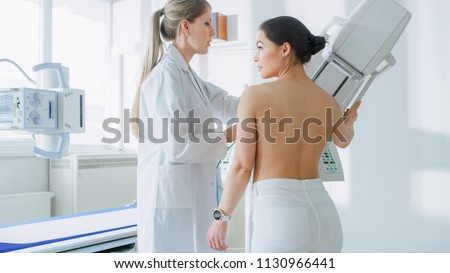 In the Hospital, Mammography Technologist / Doctor adjusts Mammogram Machine for a Female Patient. Friendly Doctor Explains Importance of Breast Cancer Prevention Screening. Modern Hospital.