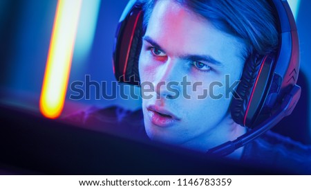Portrait of the Young Handsome Pro Gamer Playing in Online Video Game, talks with Team Players through Microphone. Neon Colored Room. e-Sport Cyber Games Internet Championship.