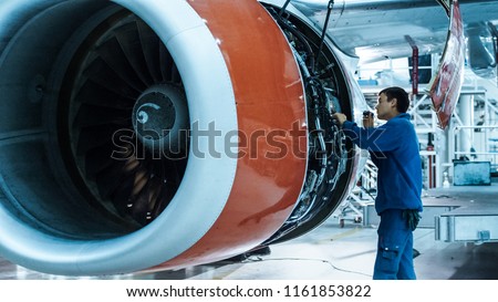 Aircraft maintenance mechanic with a flash light inspects plane engine in a hangar.