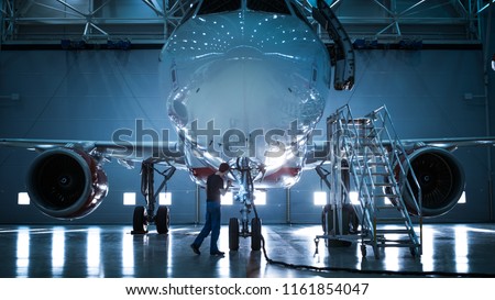 Brand New Airplane Standing in a Aircraft Maintenance Hangar while Aircraft Maintenance Engineer/ Technician/ Mechanic goes inside Cabin via Ladder/ Ramp.