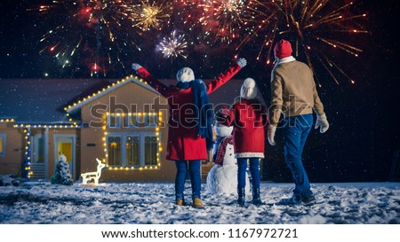Happy New Year Celebration, Young Family of Three Standing in the Front Yard Looking into the Sky In the Eveningю House Decorated with Garlands for Christmas Eve.