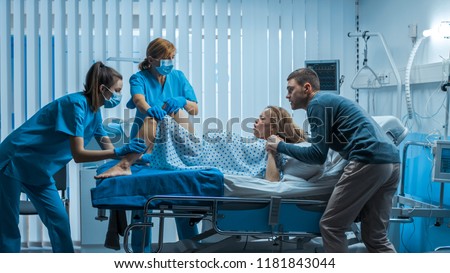 In the Hospital Woman in Labor Pushes to Give Birth, Obstetricians Assisting, Husband Holds Her Hand. Modern Delivery Ward with Professional Midwives.