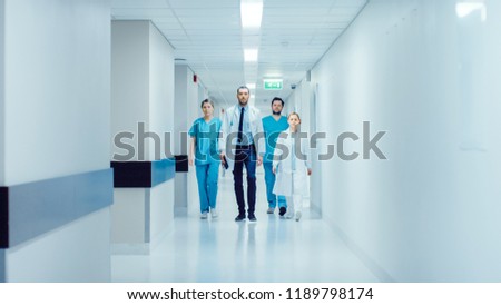 Team of Doctors, Surgeons and Nurses Walk Through Busy Hospital Hallway, They Talk about Patients, Forthcoming Surgeries and Saving Lives. Clean Modern Hospital with Professional Staff.