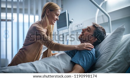 In the Hospital, Happy Wife Visits Her Recovering Husband who is Lying on the Bed. They Lovingly Embrace and Smile.