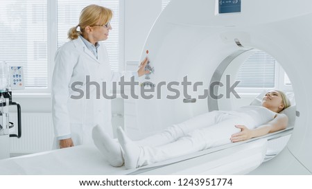 In Medical Laboratory Radiologist Controls MRI or CT or PET Scan with Female Patient Undergoing Procedure. High-Tech Modern Medical Equipment. Friendly Doctor Chats with Patient.