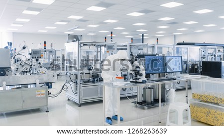 Shot of Sterile Pharmaceutical Manufacturing Laboratory where Scientists in Protective Coverall\'s Do Research, Quality Control and Work on the Discovery of new Medicine.