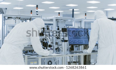 In Laboratory Scientists in Protective Clothes Doing Research, Using Microscope and Entering Data into Personal Computer. Modern Manufactory Producing Semiconductors and Pharmaceutical Items.
