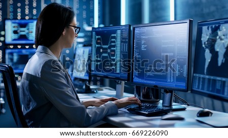 Female System Engineer Controls Operational Proceedings. In the Background Working Monitors Show Various Information.