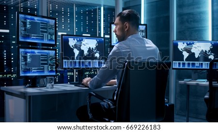 Technical Controller Working at His Workstation with Multiple Displays. Displays Show Various Technical Information. He\'s Alone in System Control Center.