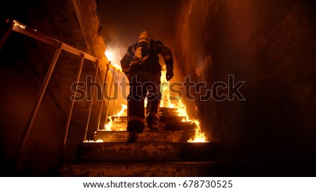 Strong and brave Firefighter Going Up The Stairs in Burning Building. Stairs Burn With Open Flames.