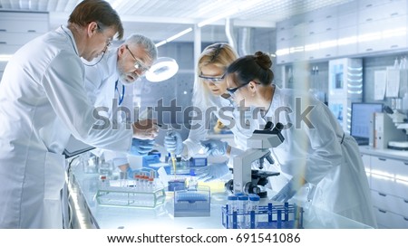Team of Medical Research Scientists Work on a New Generation Disease Cure. They use Microscope, Test Tubes, Micropipette and Writing Down Analysis Results. Laboratory Looks Busy, Bright and Modern.