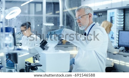 Senior Medical Research Scientist Takes Out Petri Dish with Samples from Opened Refrigerator Box. He Works in a Busy Modern Laboratory Center.