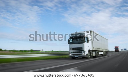 Speeding White Semi Truck with Cargo Trailer Drives on the Highway. Truck is First in the Column of Heavy Vehicles, Sun is Shining. Blur motion.
