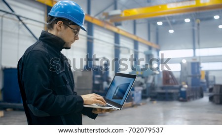 Factory worker in a hard hat is using a laptop computer with an engineering software.