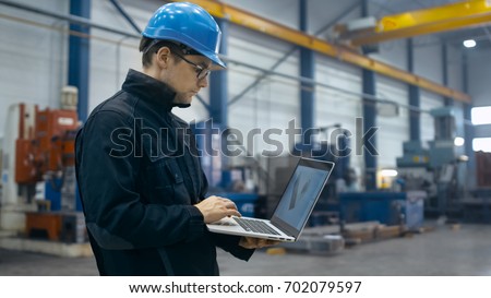 Factory worker in a hard hat is using a laptop computer with an engineering software.