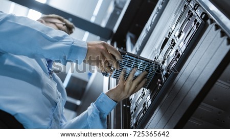 Low Angle Shot In Fully Working Data Center IT Engineer Installs Hard Drive into Server Rack. Detailed and Technically Accurate Footage.