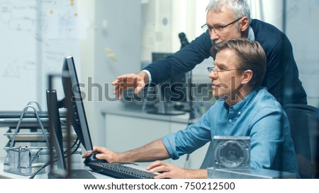 In Busy Engineering Bureau Two Senior Engineers Discussing Technical Issues over Personal Computer. Their Office Looks Minimalistic and Modern.