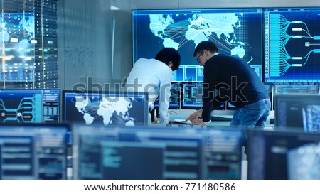 In the System Control Room Project Manage and IT Engineer Have Discussion, they\'re surrounded by Multiple Monitors with Graphics. Big Monitor Shows Interactive Logistics Map.