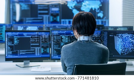 In the System Control Room Technical Operator Works at His Workstation with Multiple Displays Showing Graphics. IT Technician Works on Artificial Intelligence, Big Data Mining, Neural Network Project.