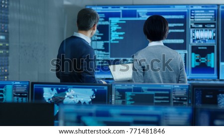 In the System Control Room IT Specialist and Project Engineer Have Discussion, they're surrounded by Multiple Monitors with Graphics. They Work in a Data Center on Data Mining.
