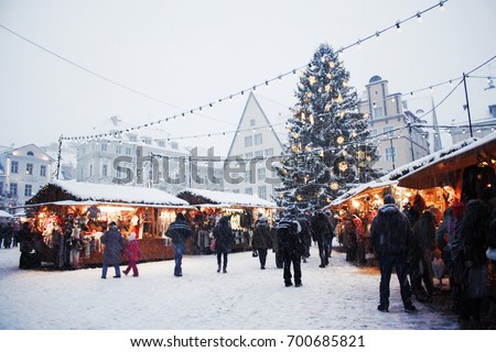 Traditional Christmas market with a Christmas tree, lights, booths and warmly dressed people at the Town Hall square in Tallinn Old Town on a snowy day in Estonia.