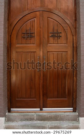 Closed double entry wood door with black wrought iron handles.