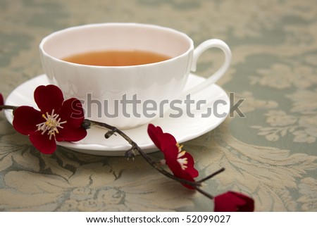 A cup of tea in a white china teacup accented with a red Japanese flower blossoms.