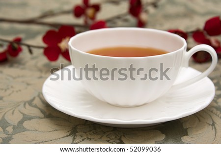 A cup of tea in a white china teacup accented with a red Japanese flower blossoms.