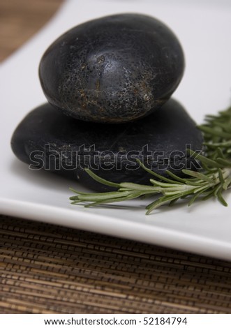 Black river stones used for spa therapy treatment with sprig of fresh rosemary herb.